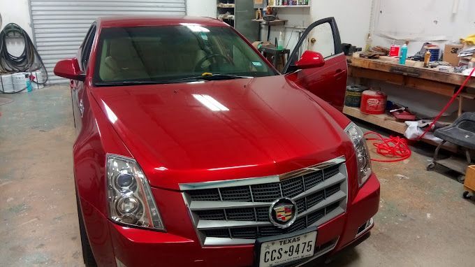 A red cadillac is parked in a garage with the door open.