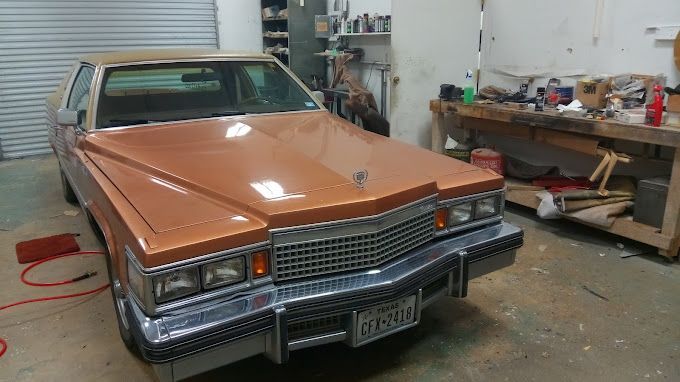A brown cadillac is parked in a garage next to a wooden workbench.