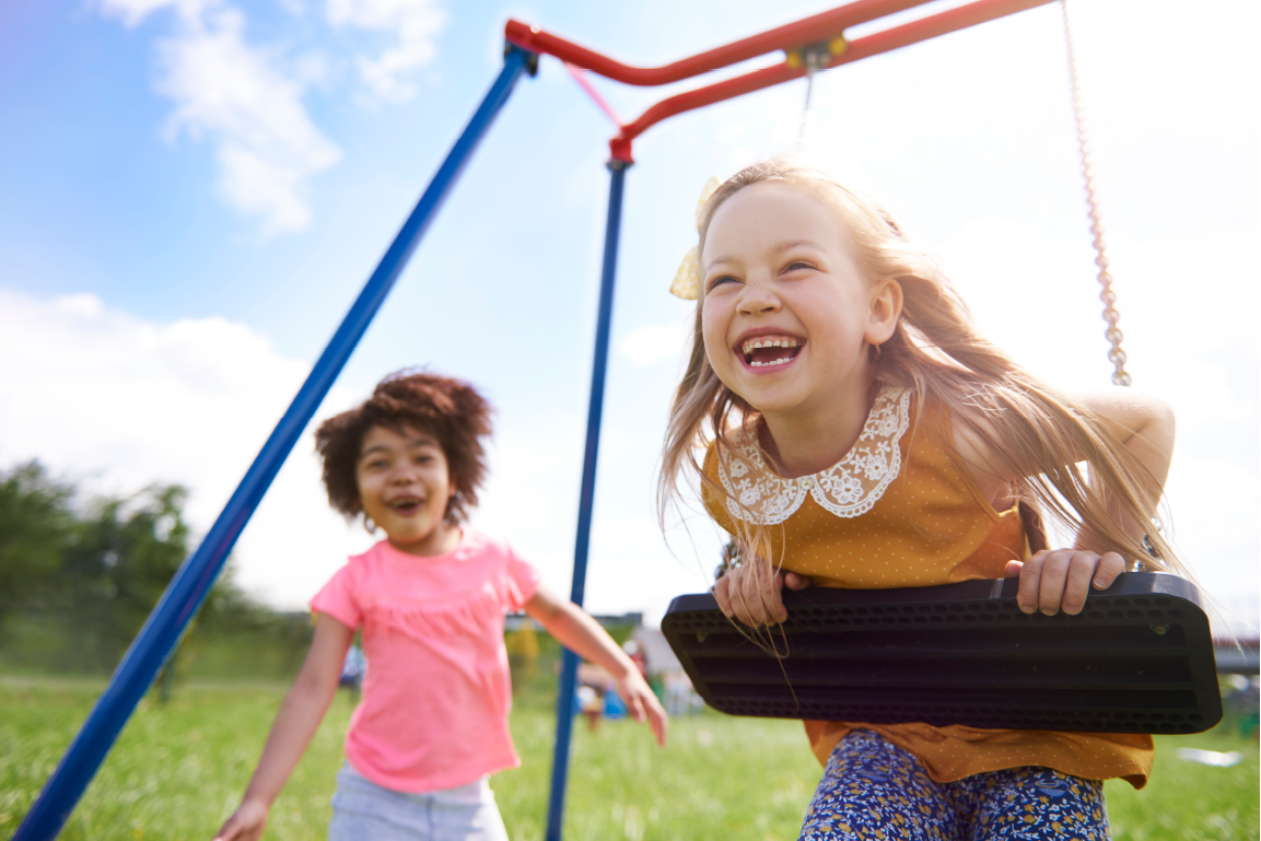 Two little girls are playing on a swing set in a park.