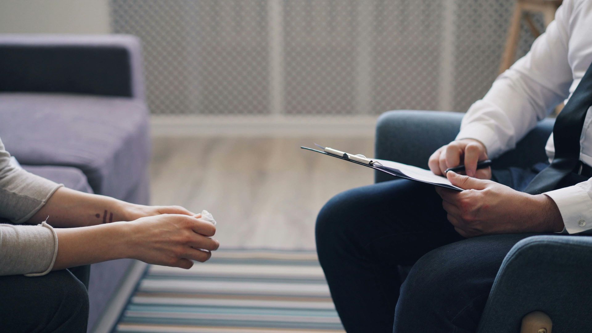 Two people in a counseling session, one taking notes while the other sits on a sofa speaking.