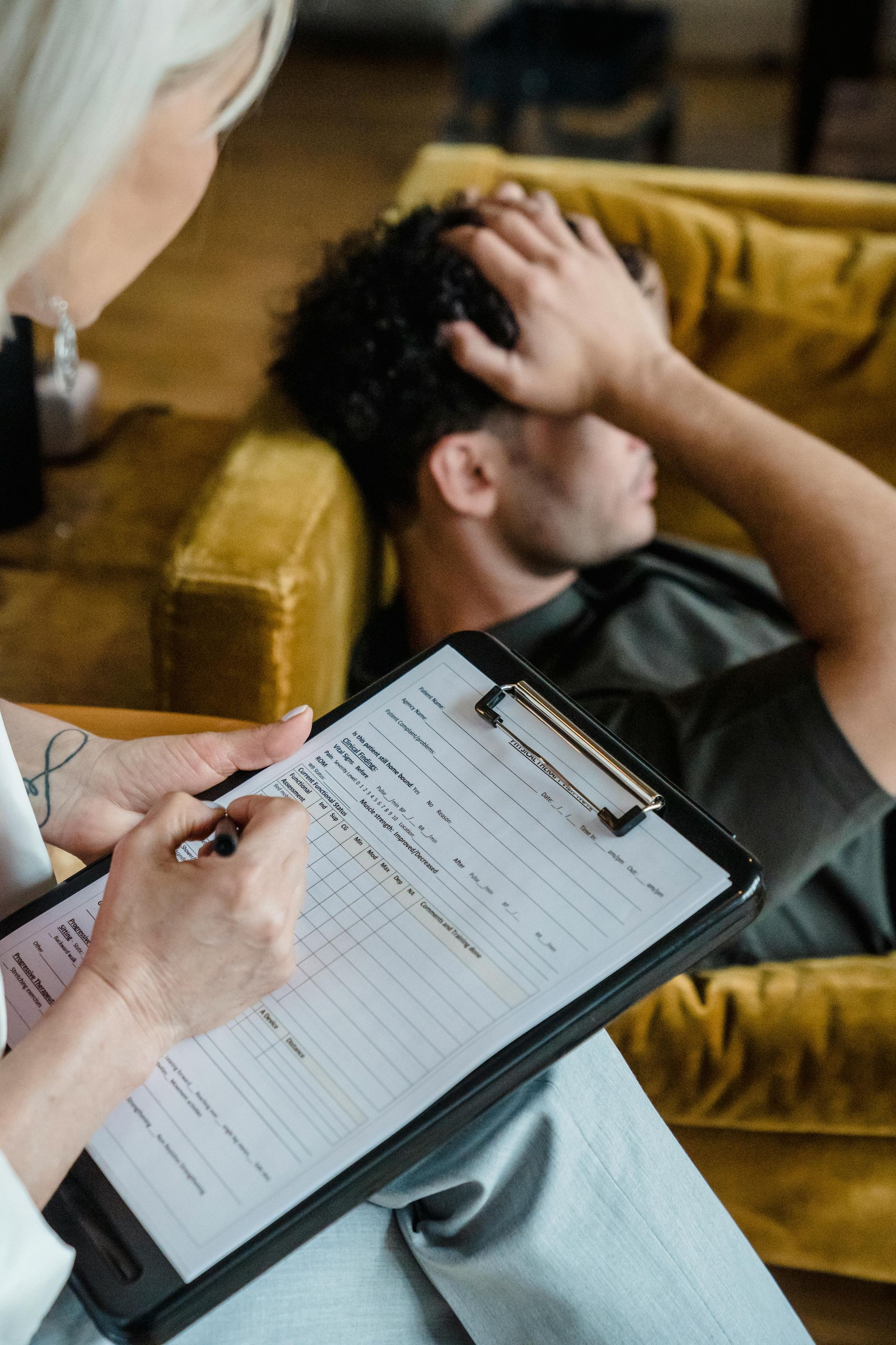 Two people seated in a counseling session, listening to an off-screen therapist in a bright office.