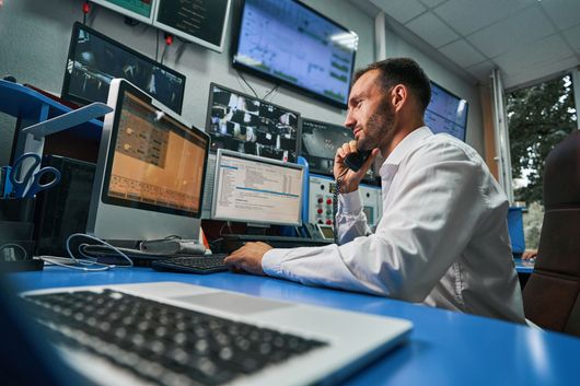 IT support technician wearing a headset and working on multiple computer screens, demonstrating technical assistance and problem-solving skills.