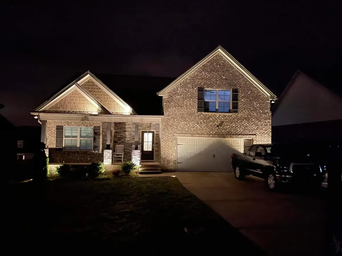 A house is lit up at night with a truck parked in front of it.