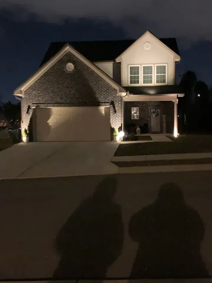 A house is lit up at night with two people standing in front of it.