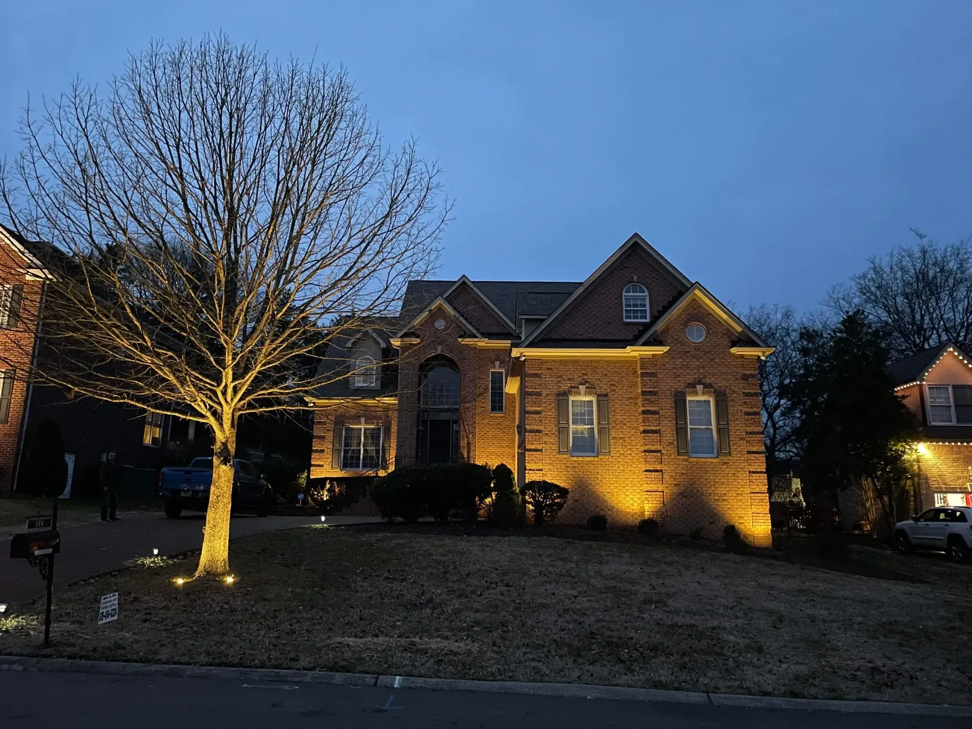 A brick house is lit up at night with a tree in front of it.