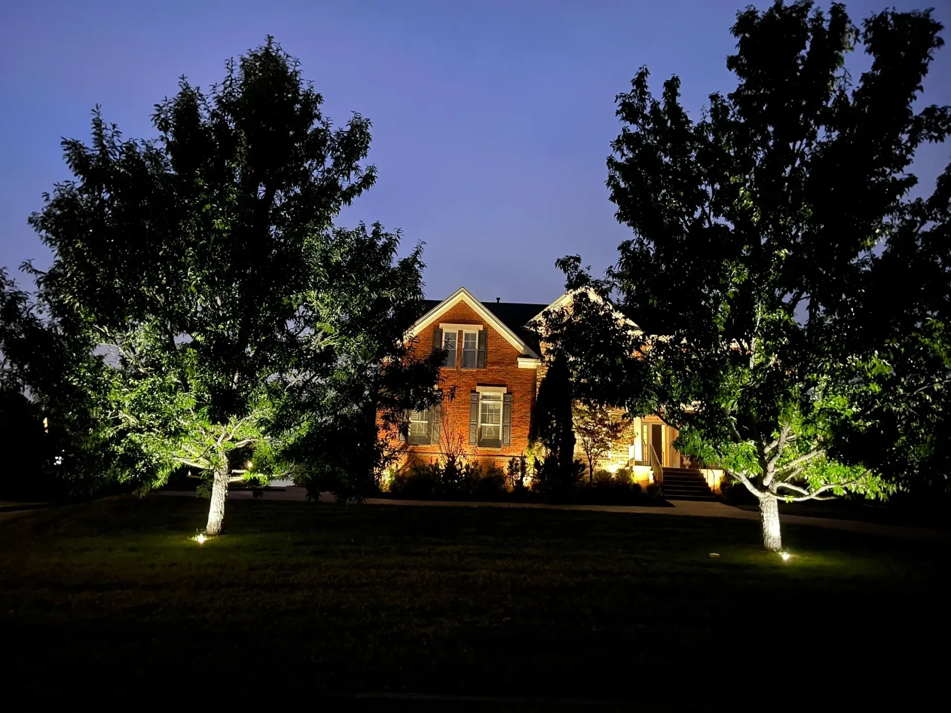 A house is lit up at night with trees in front of it