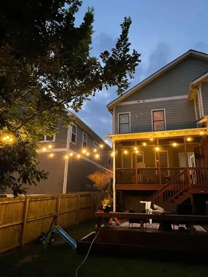 The backyard of a house with a deck and string lights.