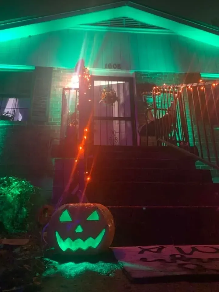 A green pumpkin is sitting in front of a house decorated for halloween.