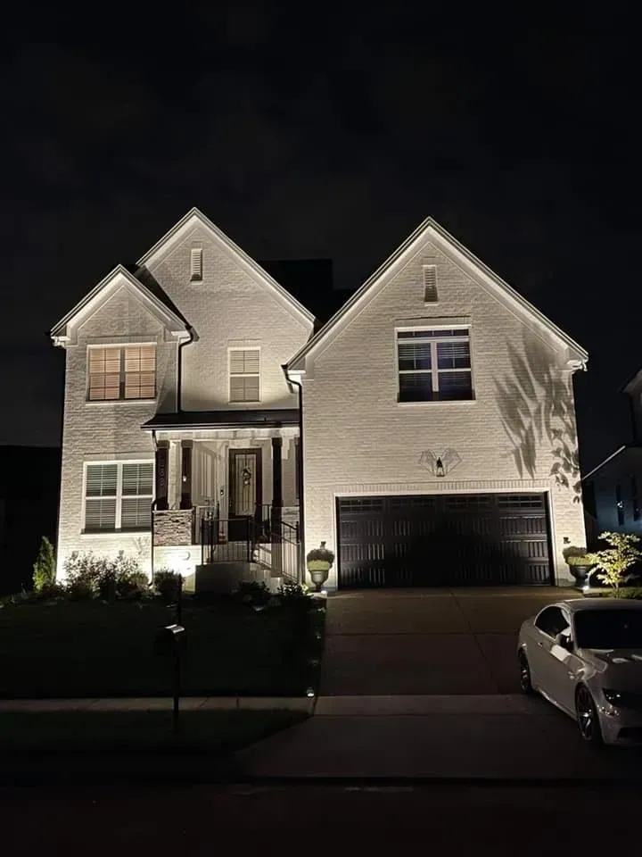 A large brick house is lit up at night with a car parked in front of it.