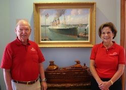 A man and a woman are standing in front of a painting of a ship.