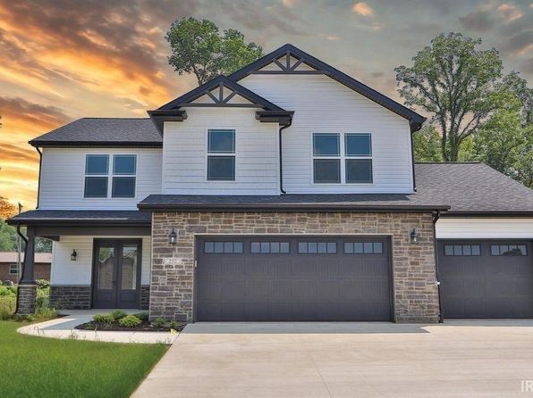 Two-story house with white siding, stone facade, and dark gray garage doors under a sunset sky.