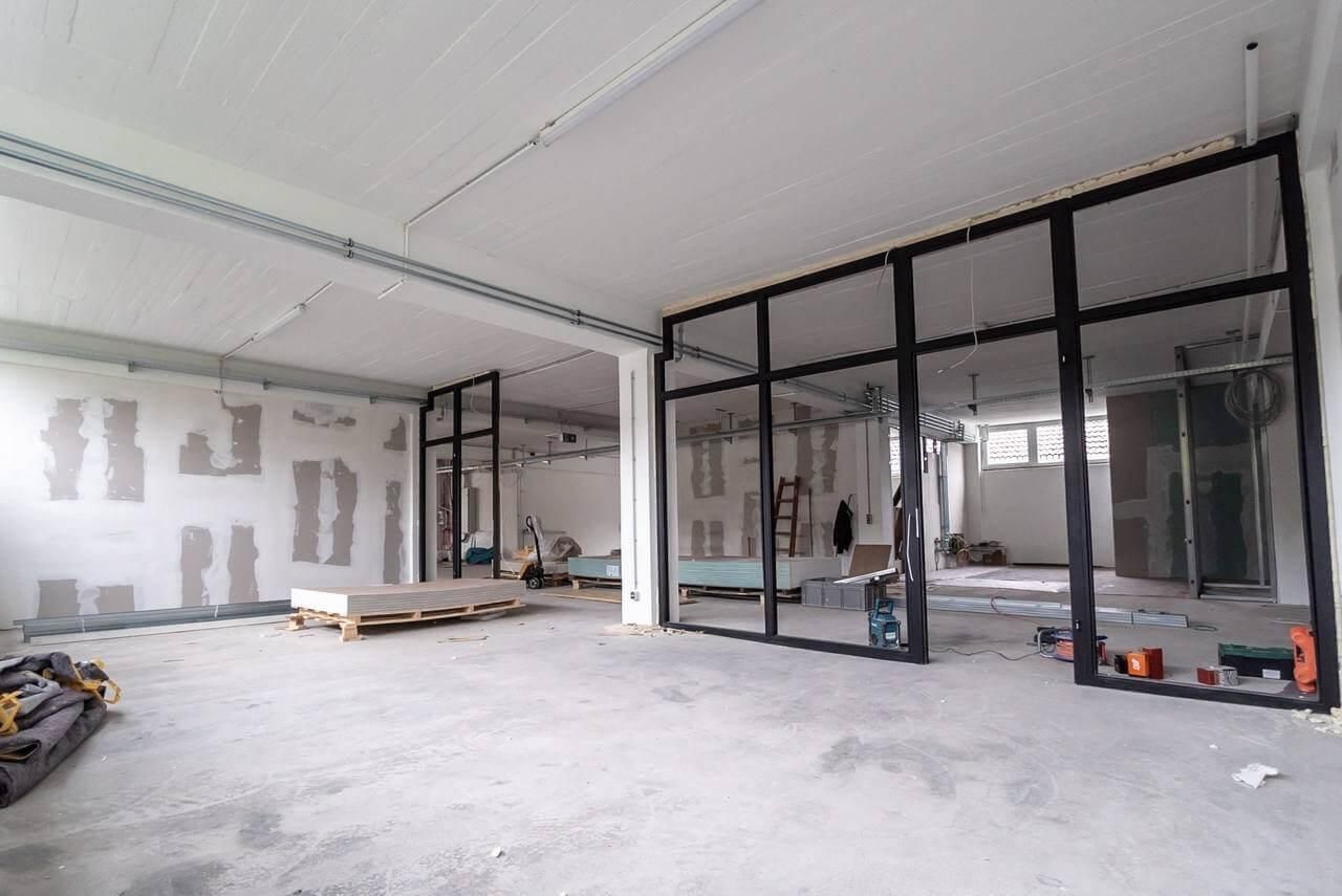 Interior view of an unfinished commercial space with glass and black metal dividers. Drywall partially installed on walls.