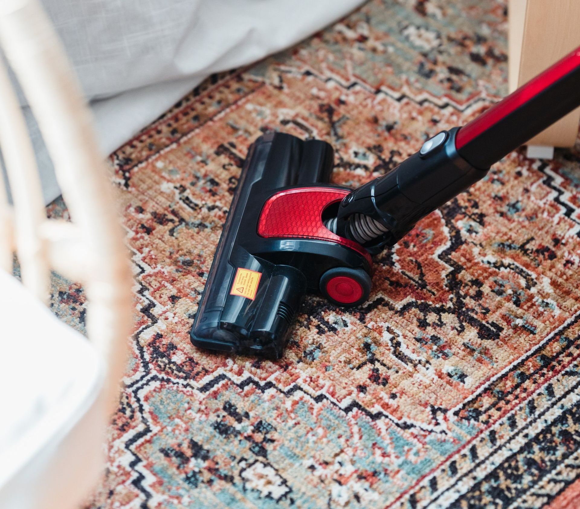 A person using a vacuum cleaner to meticulously clean an intricate rug with a pattern of vibrant colors and delicate designs.