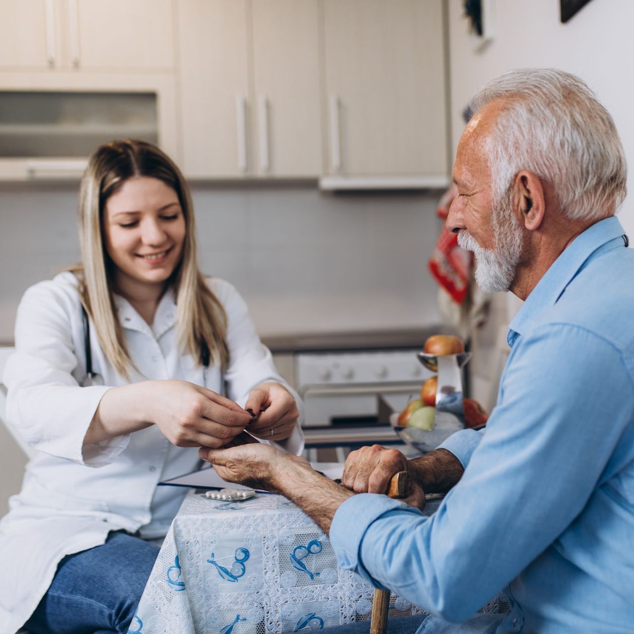 A medical professional examining an older adult's wrist indoors, smiling.