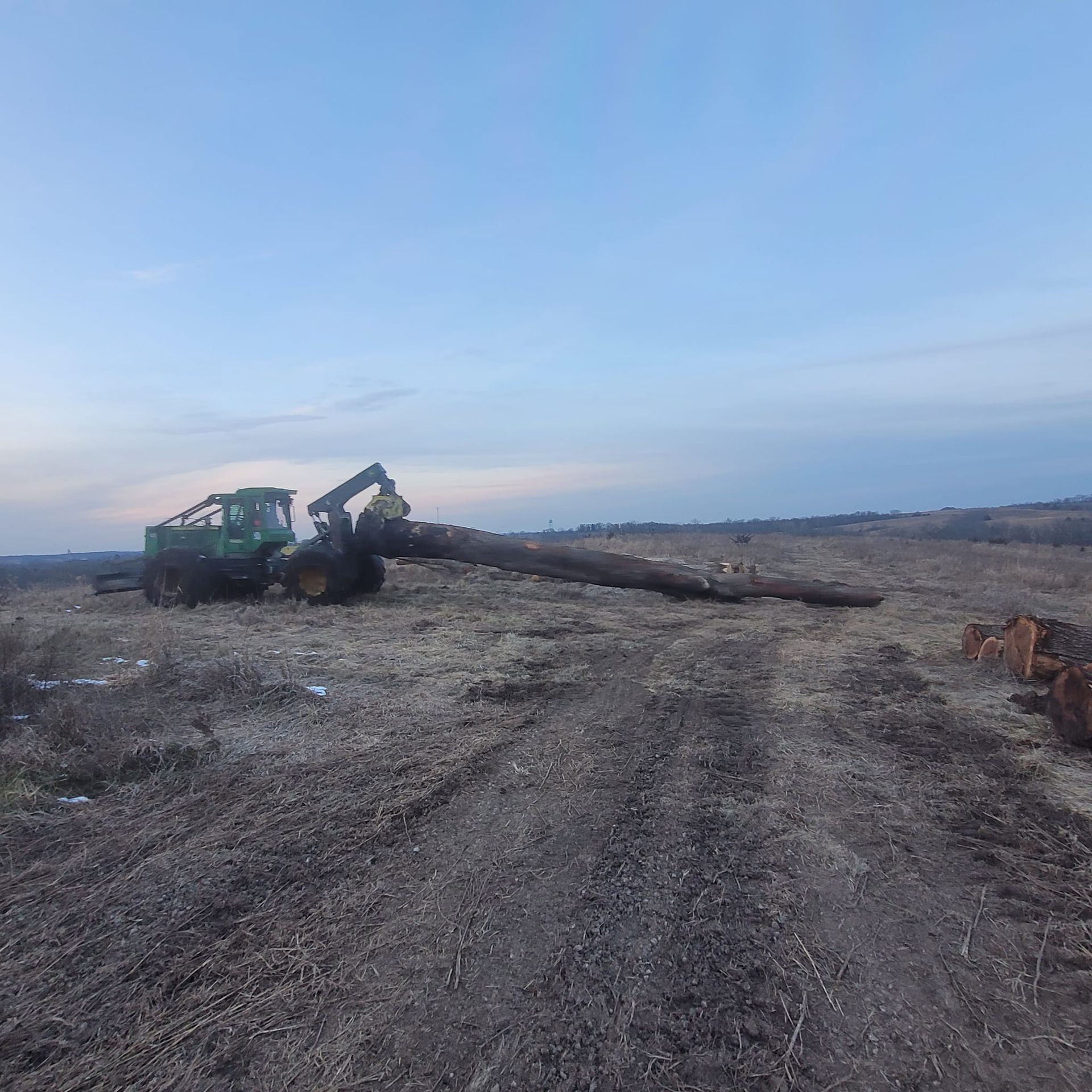A large log is being lifted by a tractor in a field.