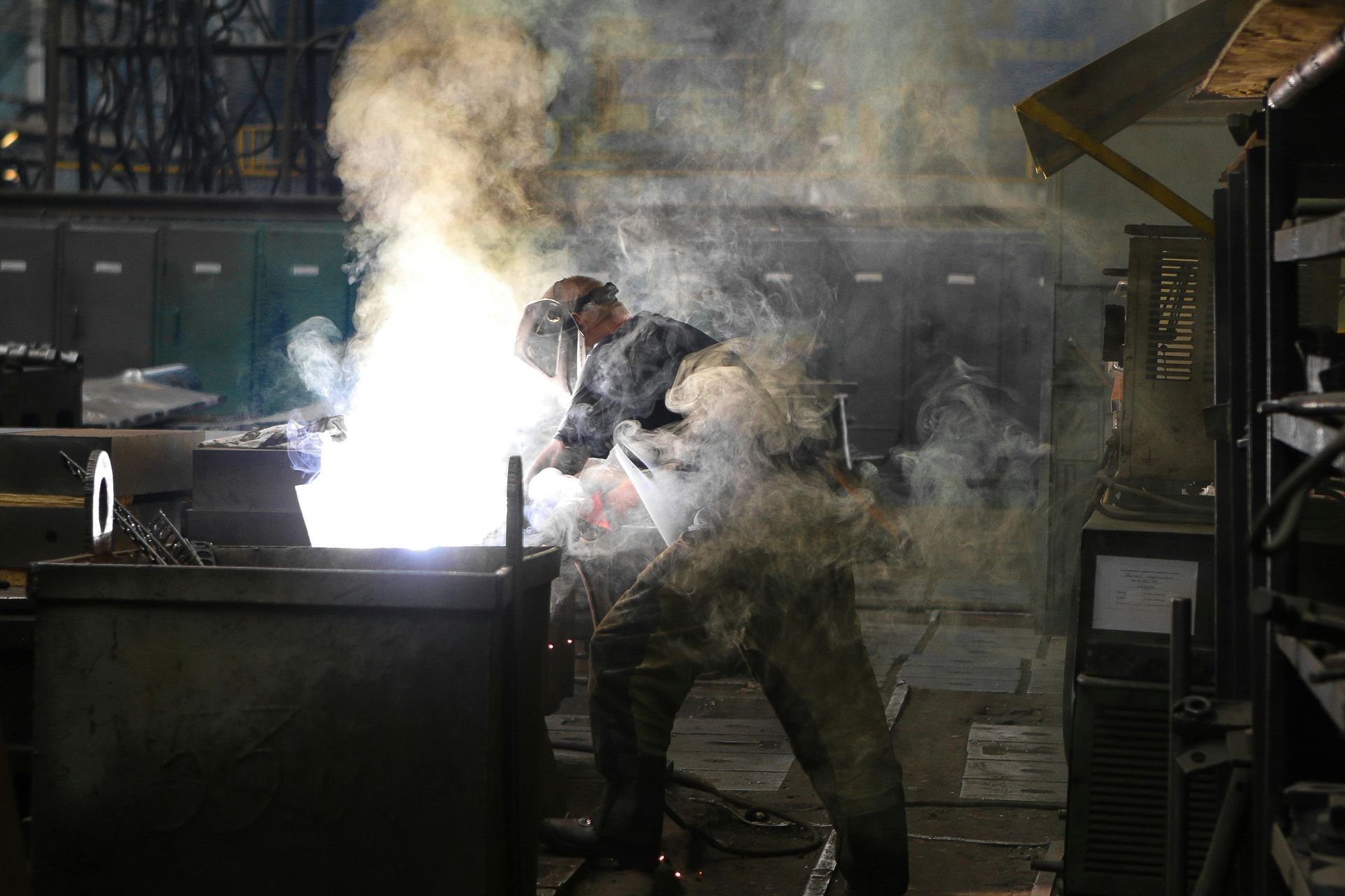 A man is welding a piece of metal in a factory.