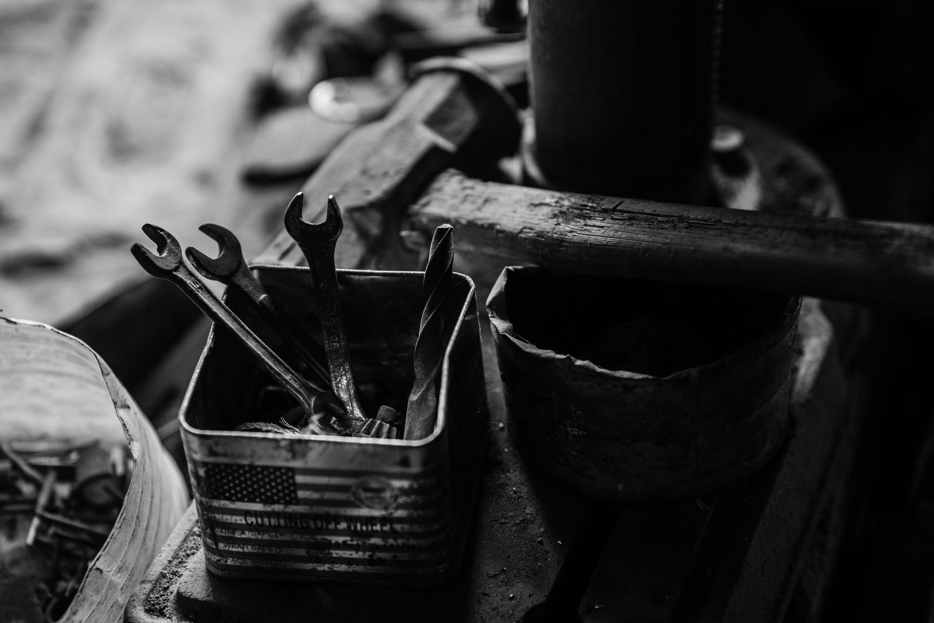 A black and white photo of a bucket of wrenches and a hammer.