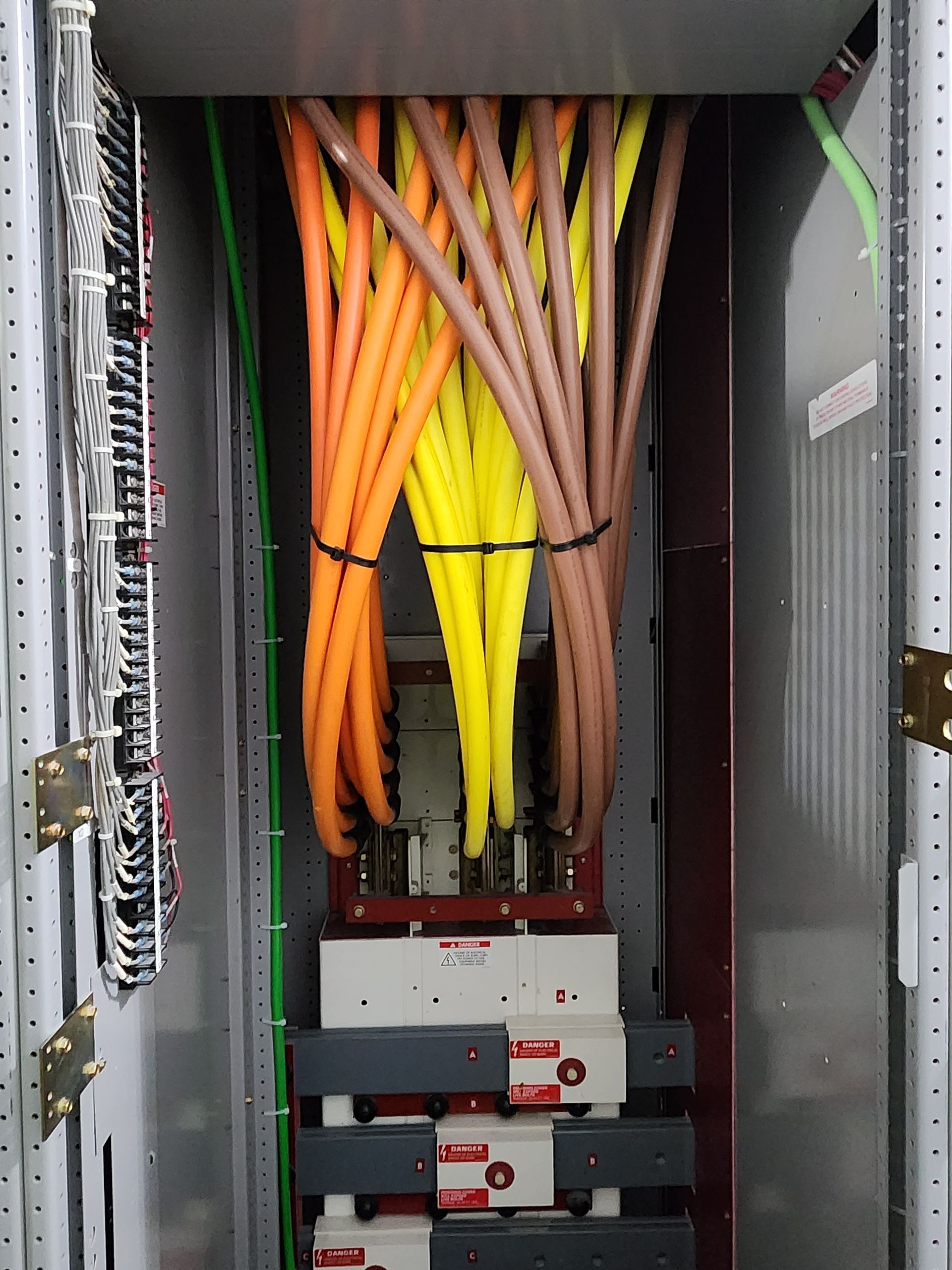 Electrical cabinet with bundled orange, yellow, and brown wires leading to circuit breakers.