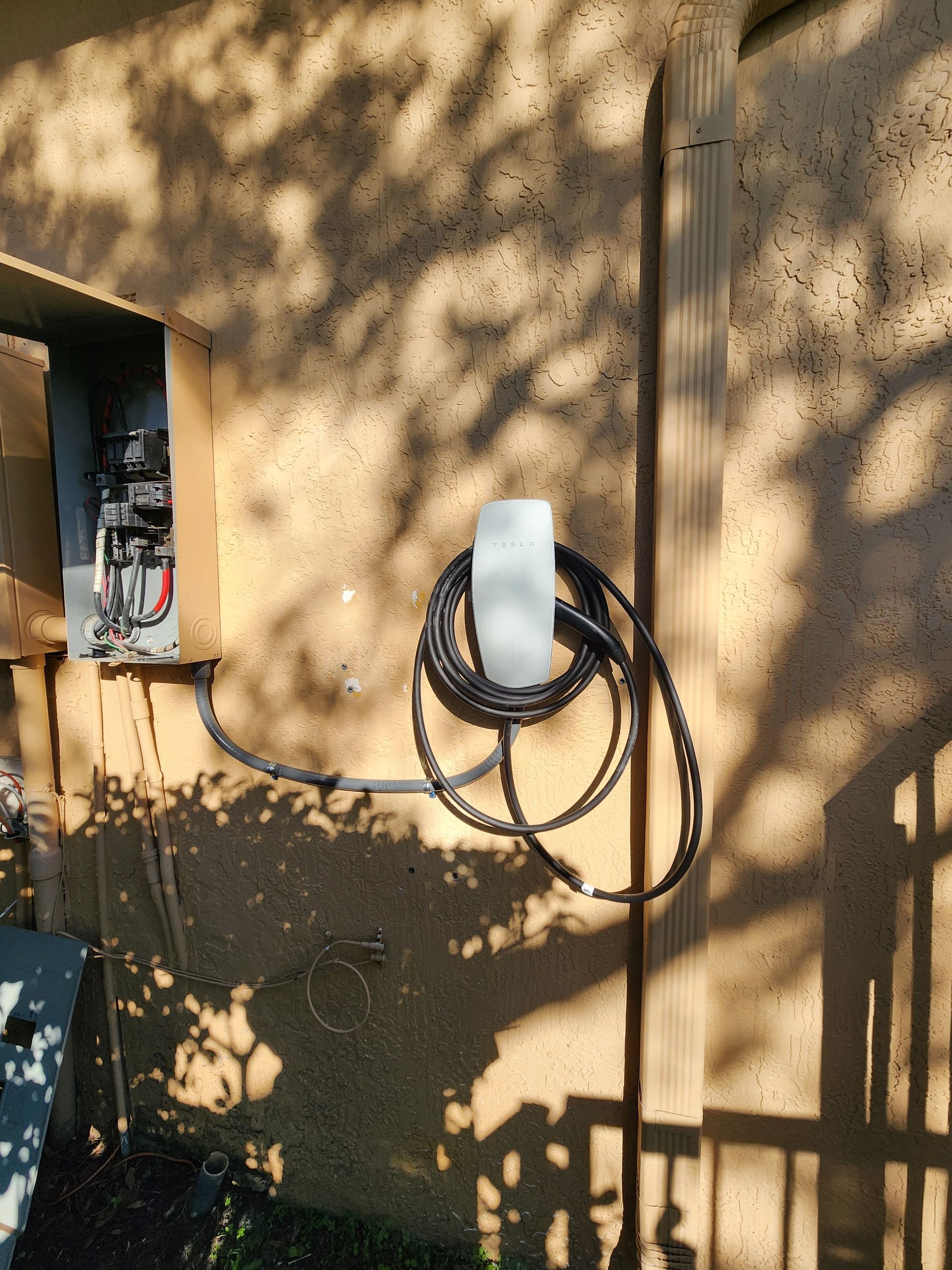 Electric vehicle charger mounted on a stucco wall next to an electrical panel.