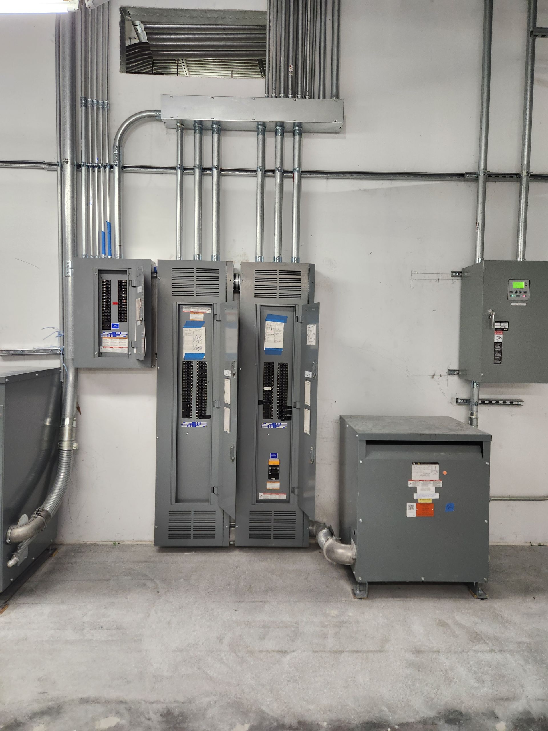 Electrical panels and transformer mounted on a gray wall. Conduit and wiring are visible.