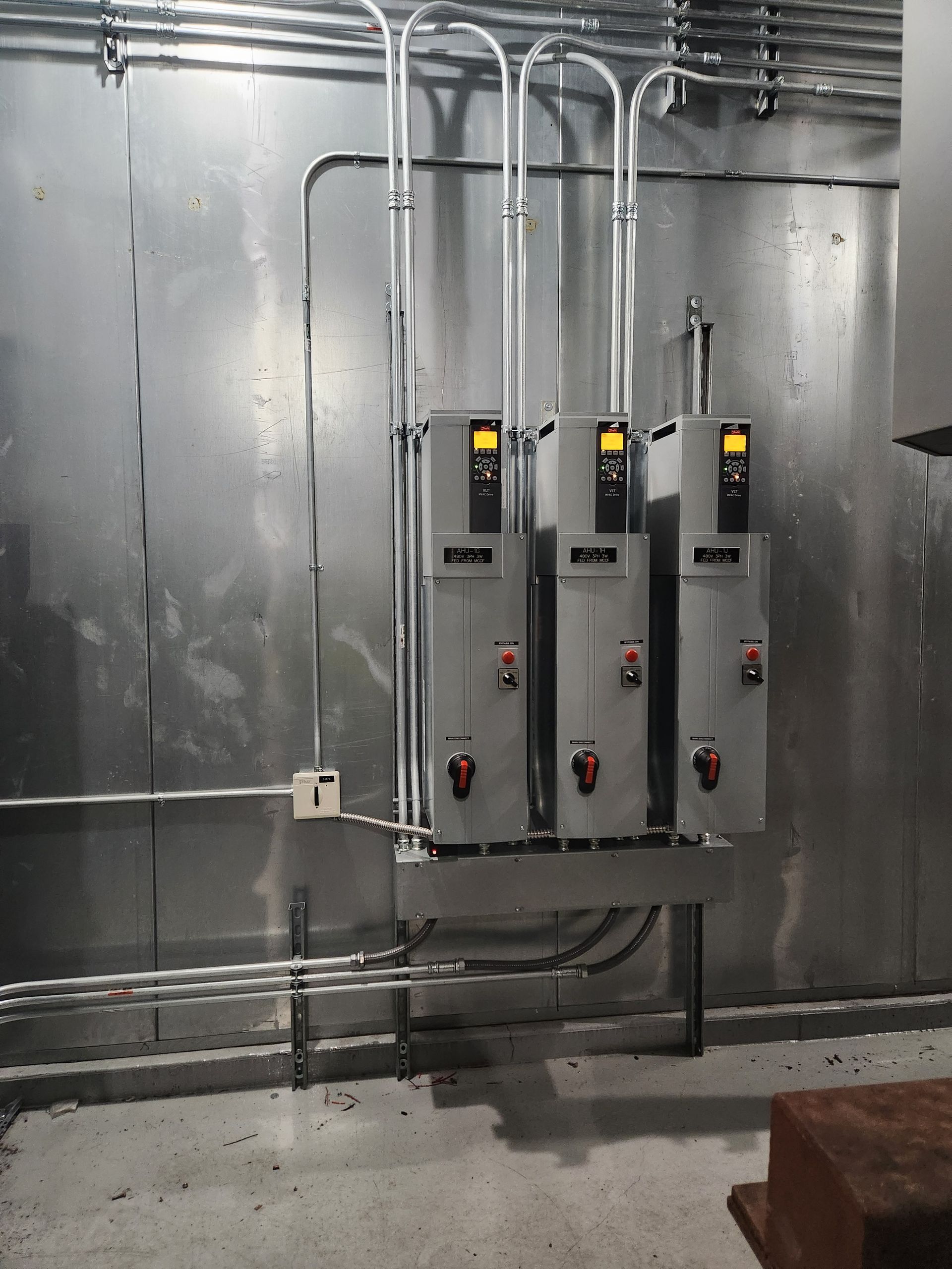 Three electrical control boxes mounted on a metal wall with conduit running overhead.