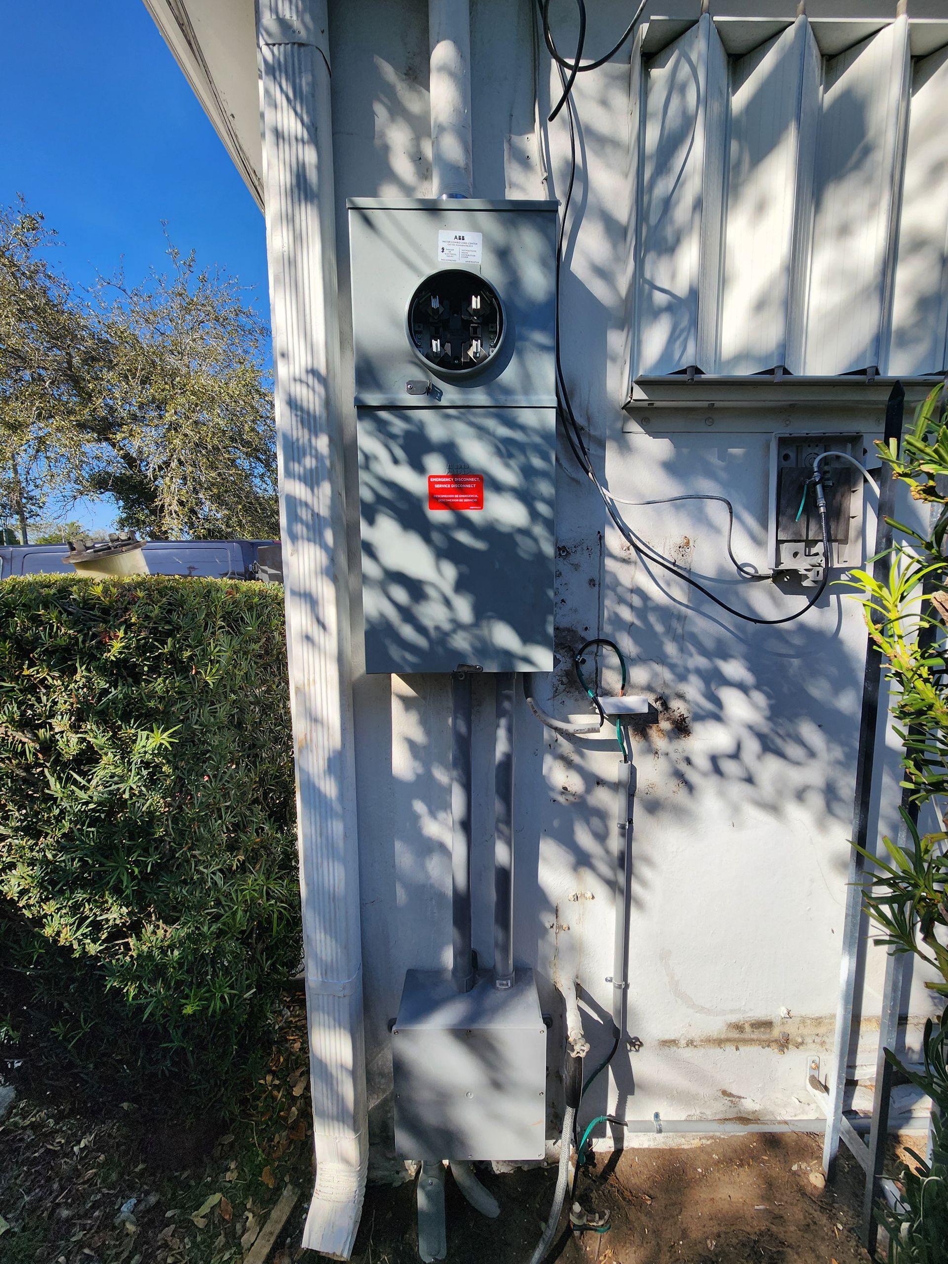 Exterior electrical panel on a white building, with meter, breaker box, and conduit.