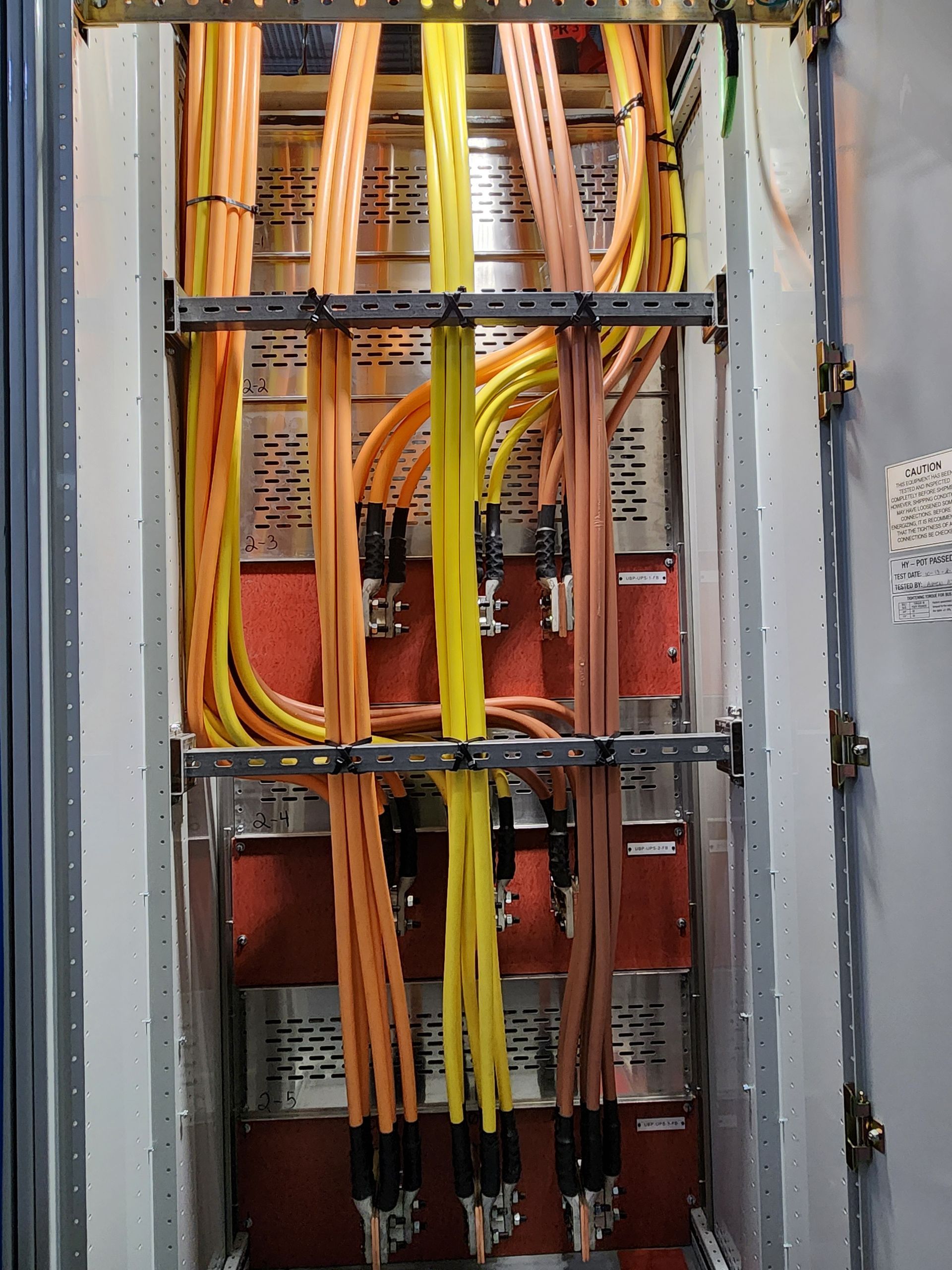 Electrical panel with orange, yellow, and black cables, secured with metal brackets.