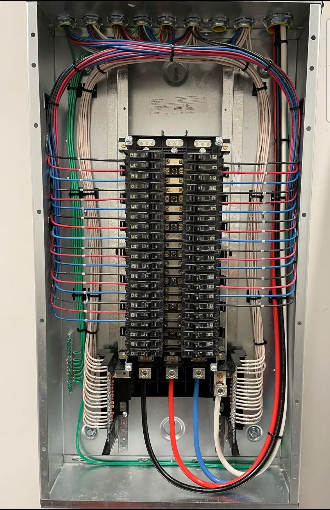 Electrical panel with numerous colored wires neatly arranged. Black circuit breakers are visible.