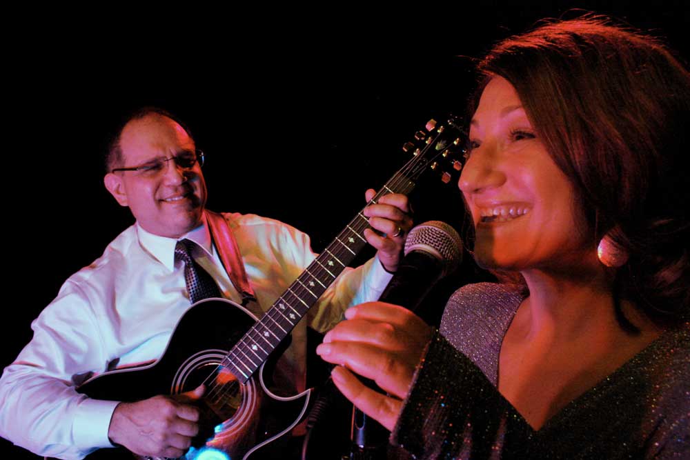 A man is playing a guitar and a woman is singing into a microphone.
