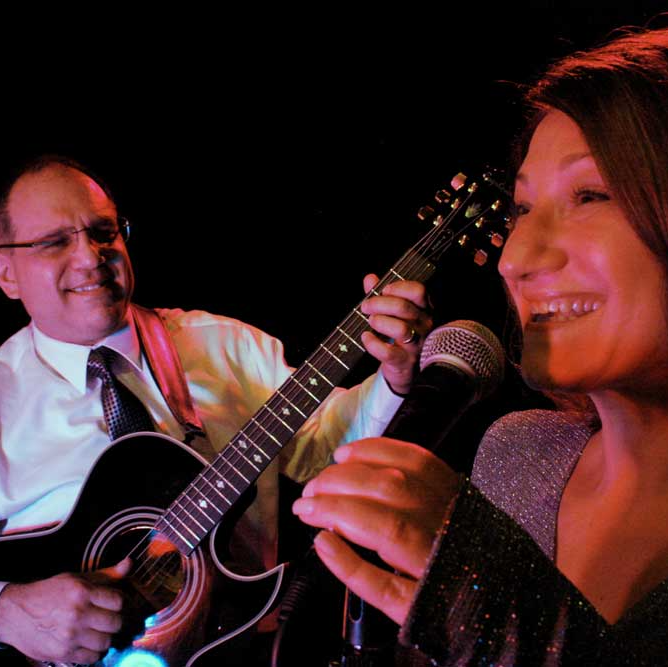 A man playing a guitar next to a woman singing into a microphone