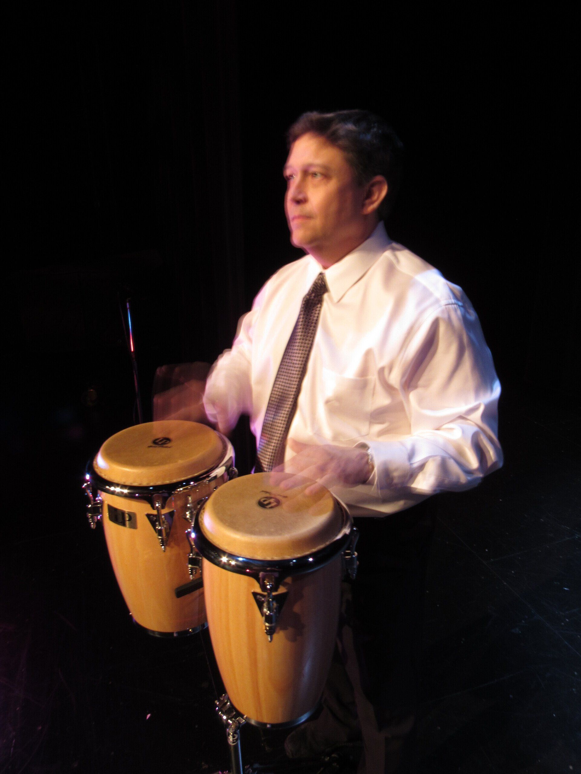 A man in a white shirt and tie is playing drums