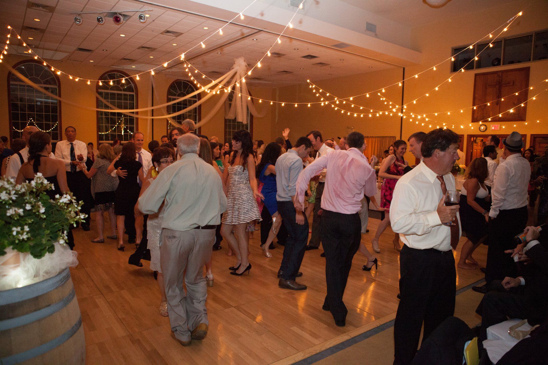 A large group of people are dancing in a room with string lights hanging from the ceiling