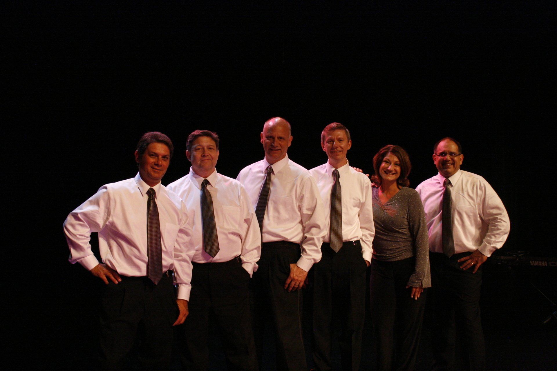 A group of men and women are posing for a picture in front of a black background.