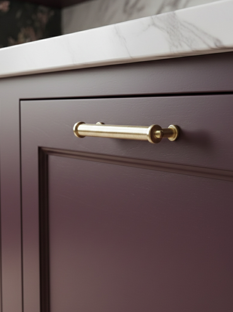 Primer plano de una puerta de armario color burdeos con tirador dorado, colocada sobre una encimera de mármol.