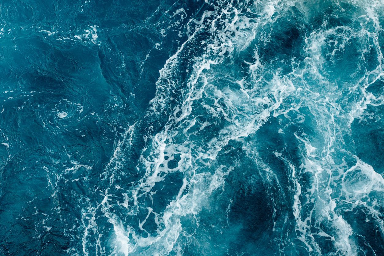 Turbulent ocean water, shades of blue and white, churning surface.