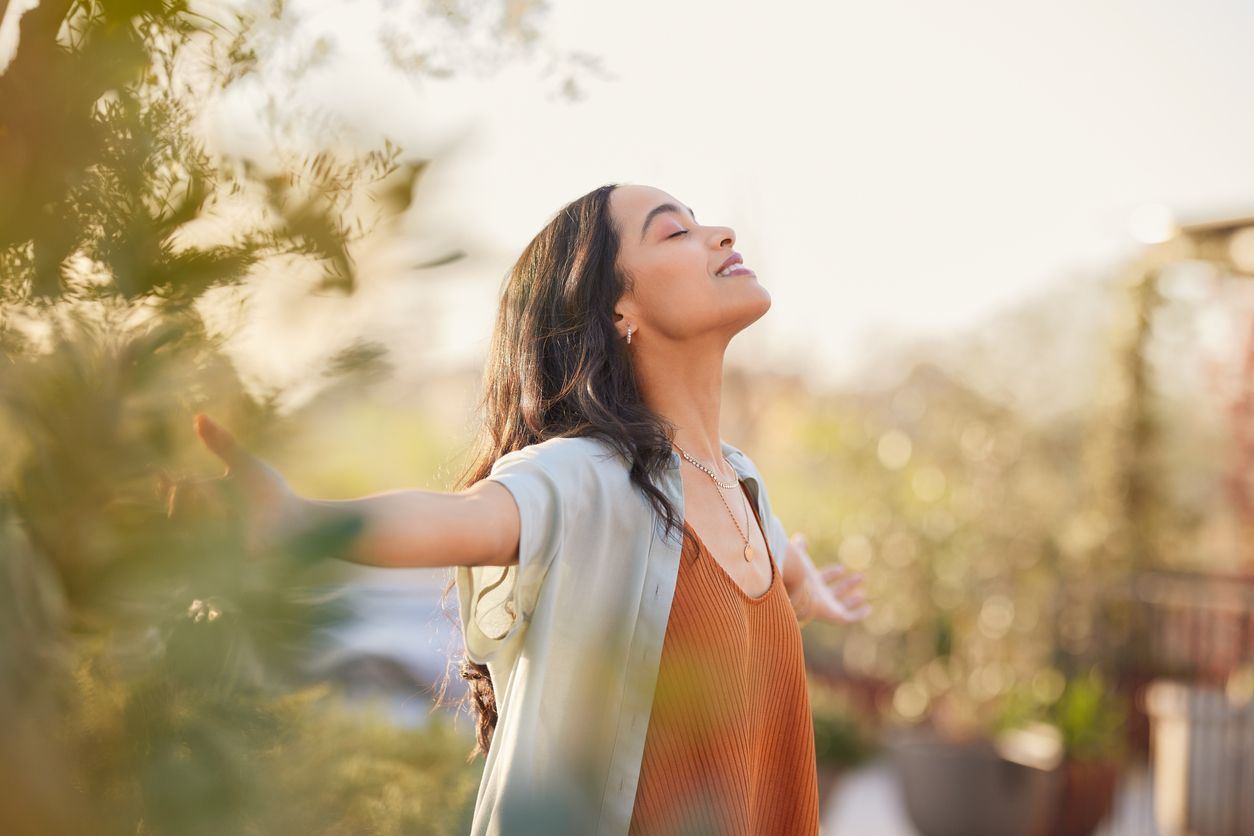 Woman with arms outstretched, eyes closed, basking in sunlight; outdoors.