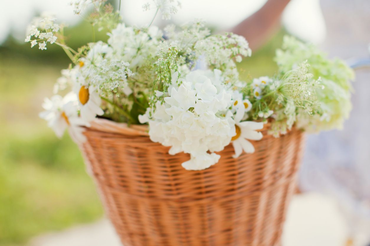 Wicker basket overflowing with white and yellow wildflowers, held by a person outdoors.