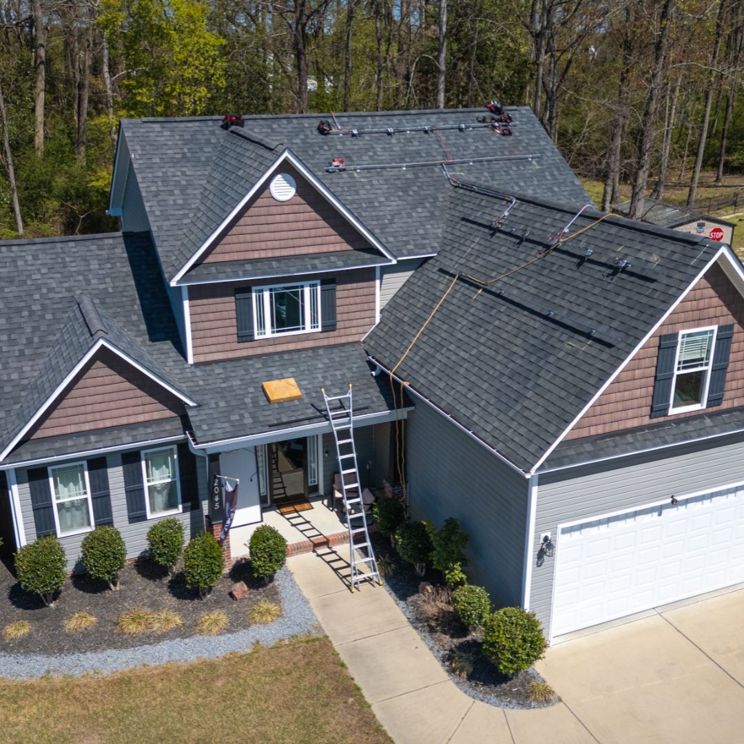 House with dark gray roof, brown siding, and landscaping. A ladder leans against the entrance.