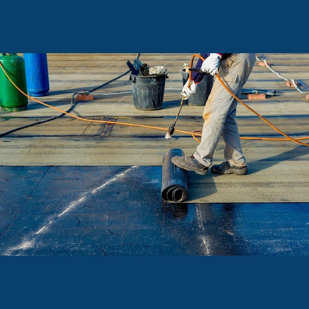 Roofer applying a rolled membrane roof with a torch on a flat surface.