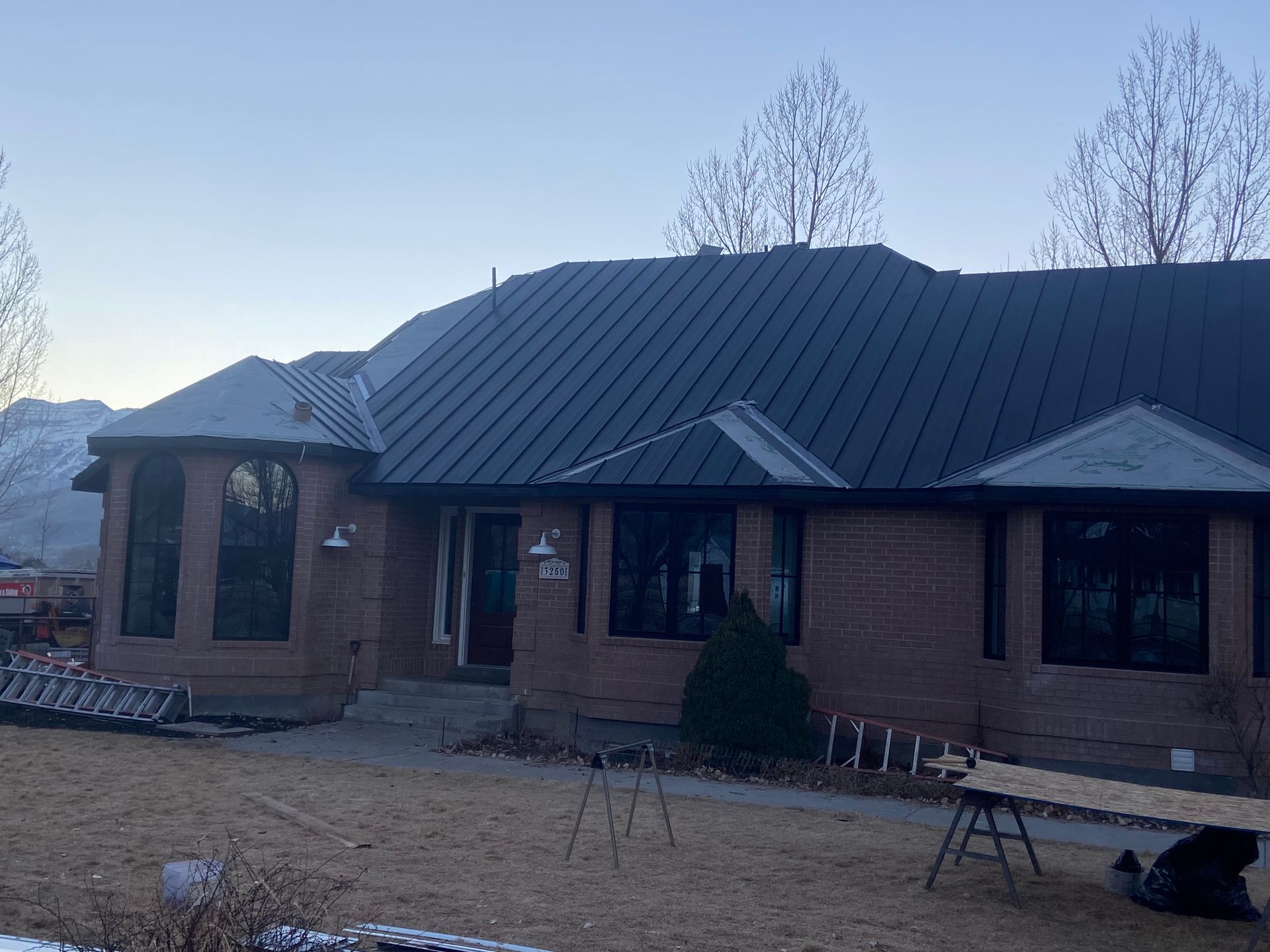 Brick house with dark roof, windows, and front door. Cloudy sky, brown lawn, and bare trees.