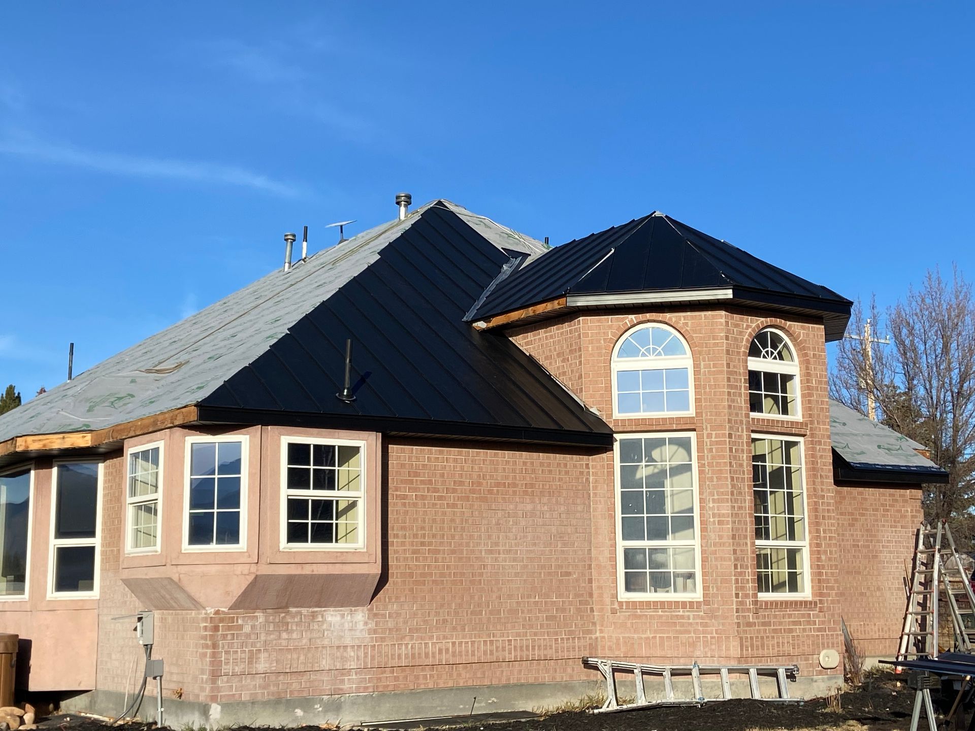 Brick house under construction with black roof and arched windows against a blue sky.