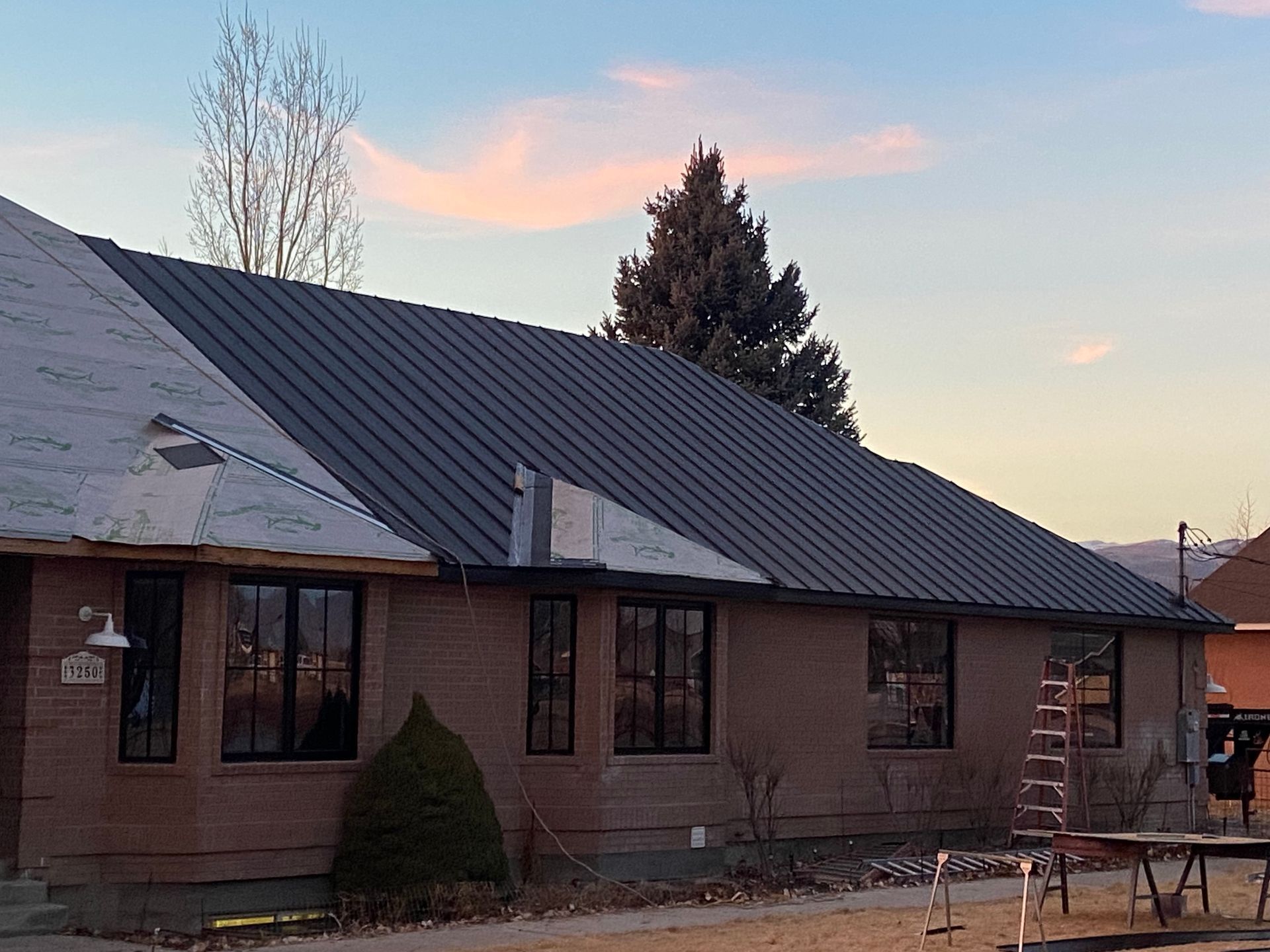 House with a dark metal roof under construction; pink and blue sky.