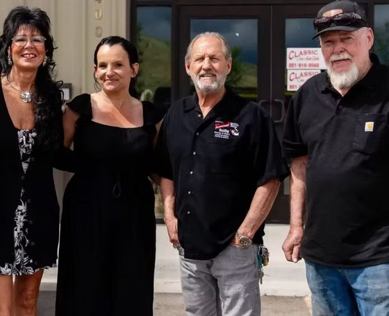 Four people in front of a building; two women and two men. All are wearing black and smiling.
