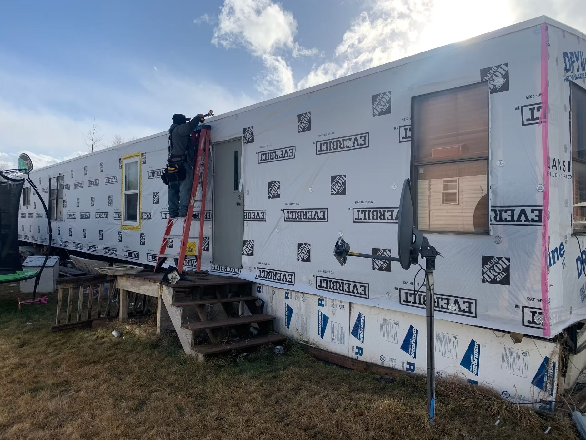 Person on ladder working on the side of a mobile home; covering with protective material.