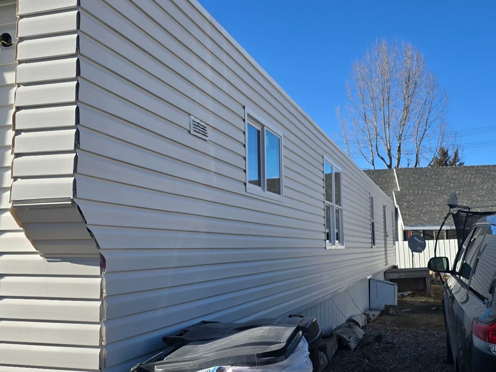 Side view of a light beige mobile home with several windows, against a blue sky.