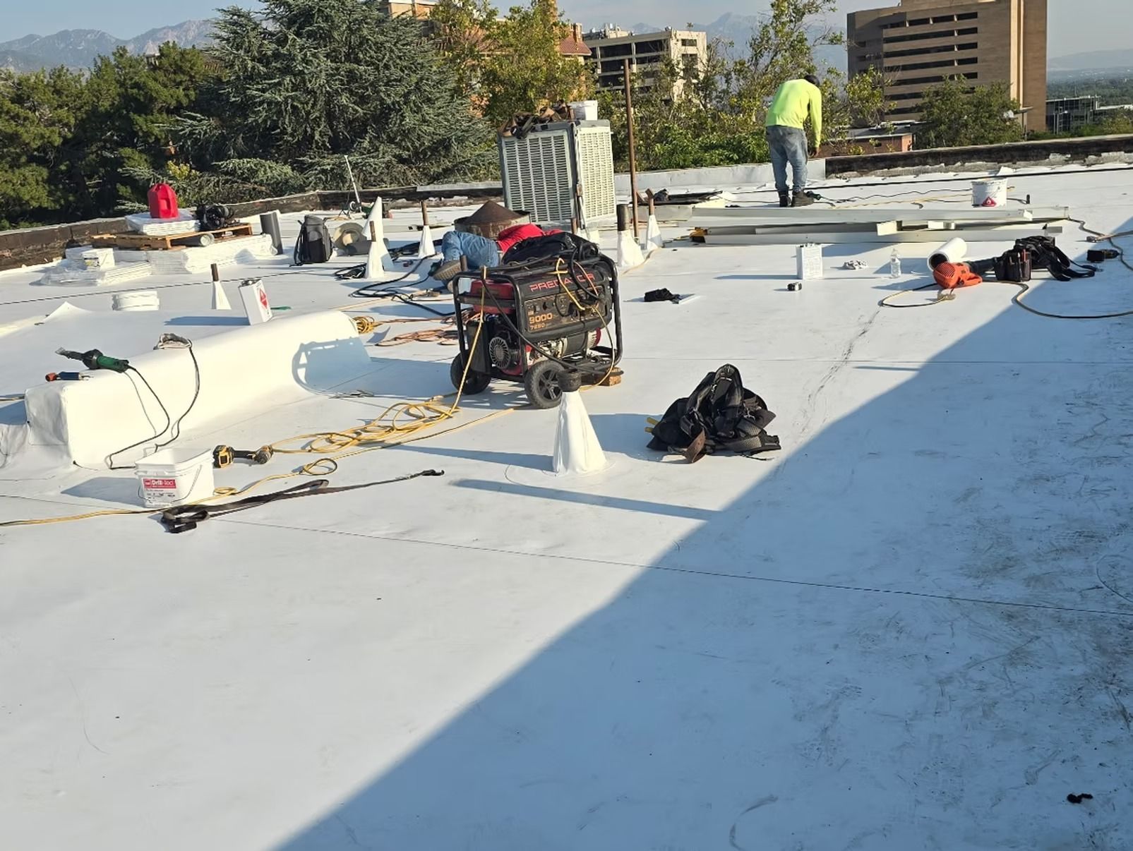 Workers on a white roof with equipment, under a sunny sky.