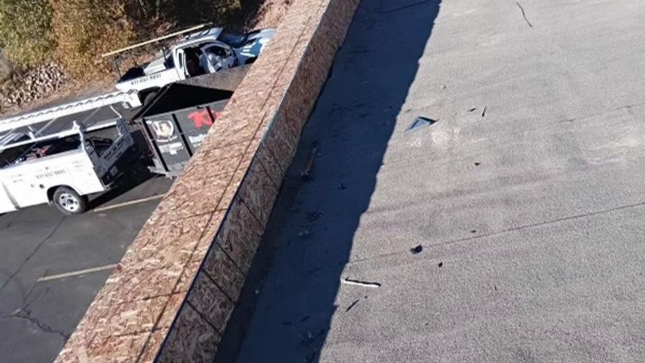 View from above of a roof with a wooden border.  A dumpster and service vehicles are parked nearby.