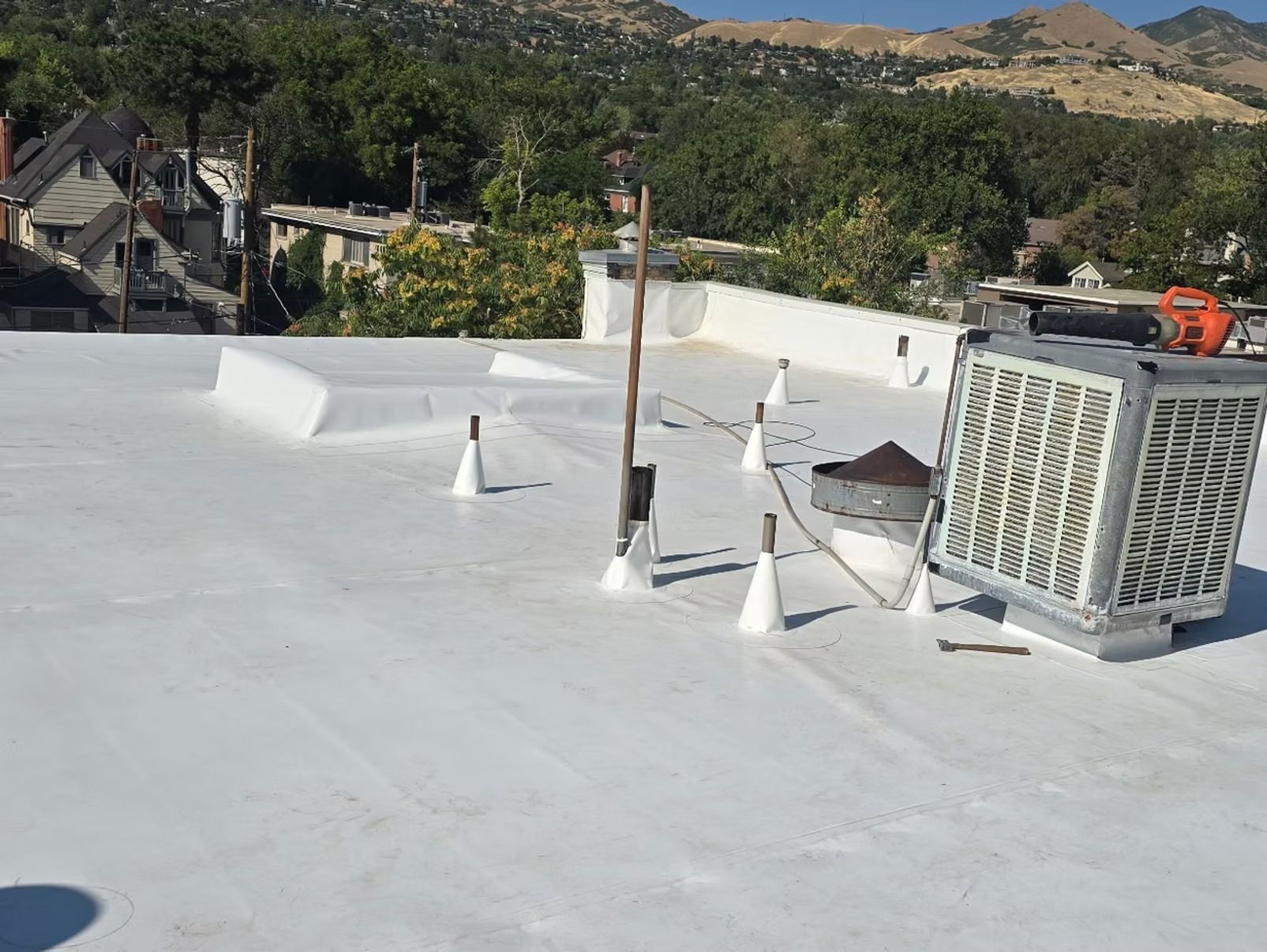 White flat roof with vents and a large air conditioning unit. Mountain backdrop.