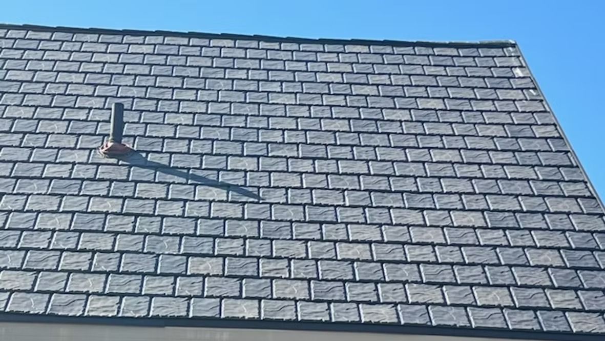 Gray slate roof with vent pipe against a blue sky.
