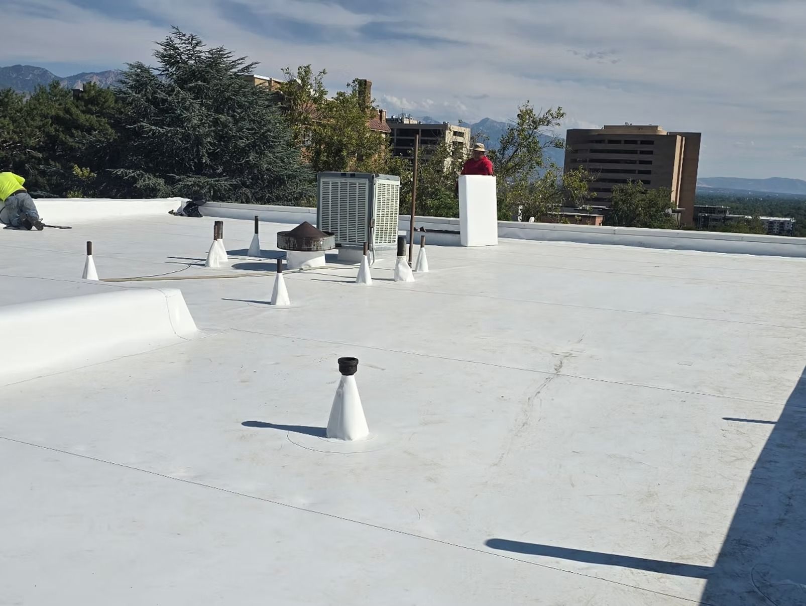 White roof with various vents, a person on it, and city buildings in the background.